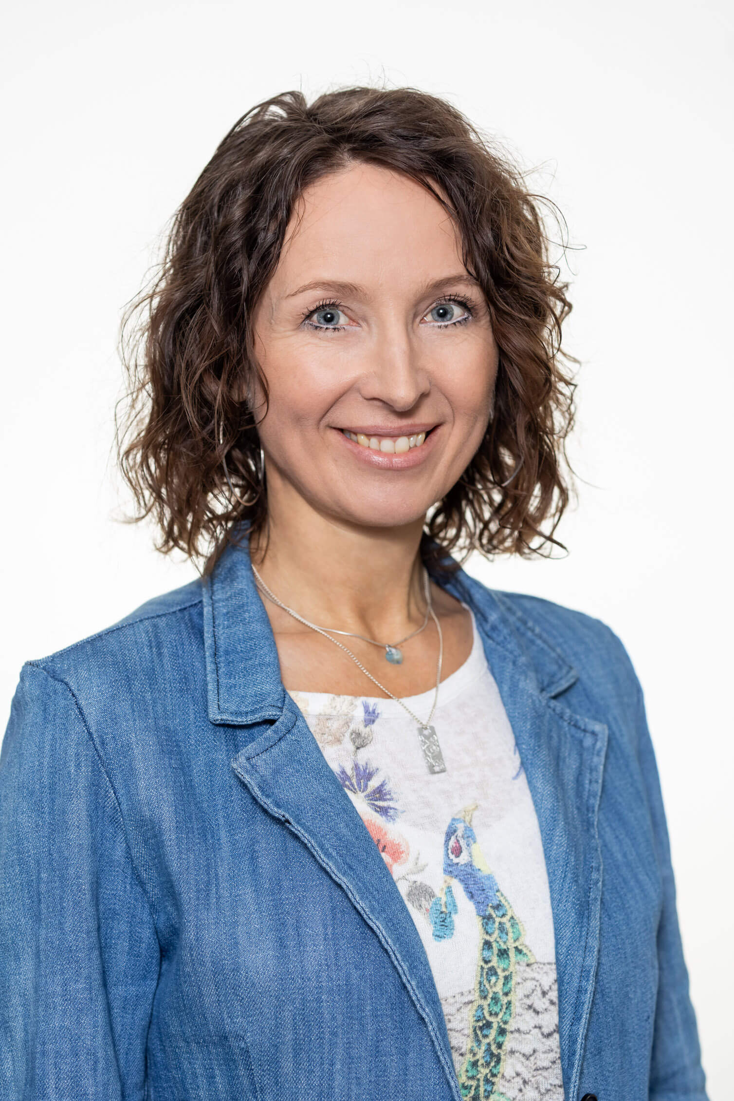 Frau Moser mit lockigem Haar, Jeansjacke und Halsketten vor hellem, Shirt mit Pfauenmotiv, Killer Entsorungsfirma