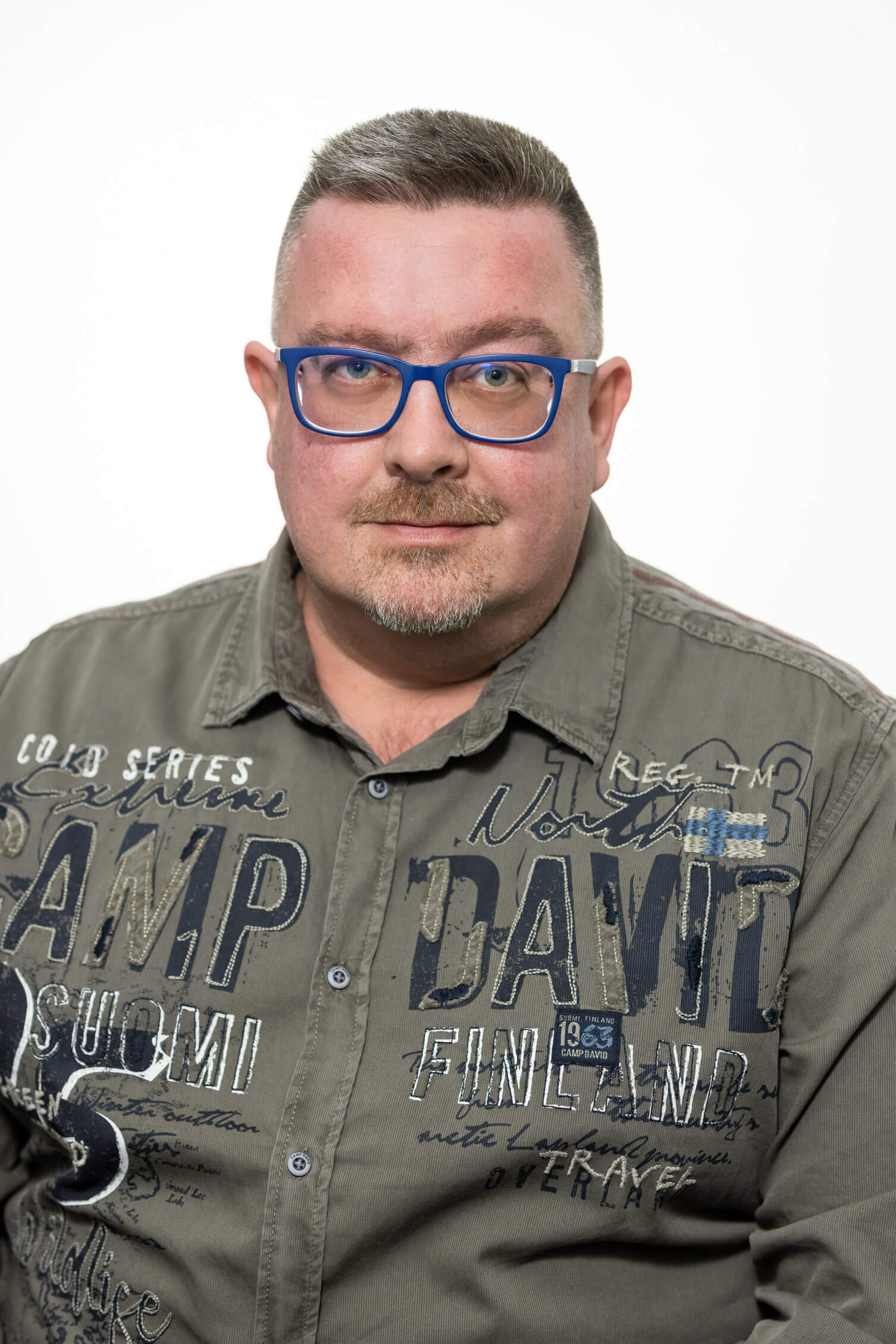 Herr Rakic mit blauen Brillengestell und grauem Hemd mit großen Aufdrucken, Killer Entsorungsfirma